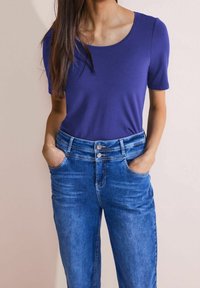 Lila kortärmad topp med rundad halsringning, parat med ljusblå denimjeans med knäppning och framfickor.