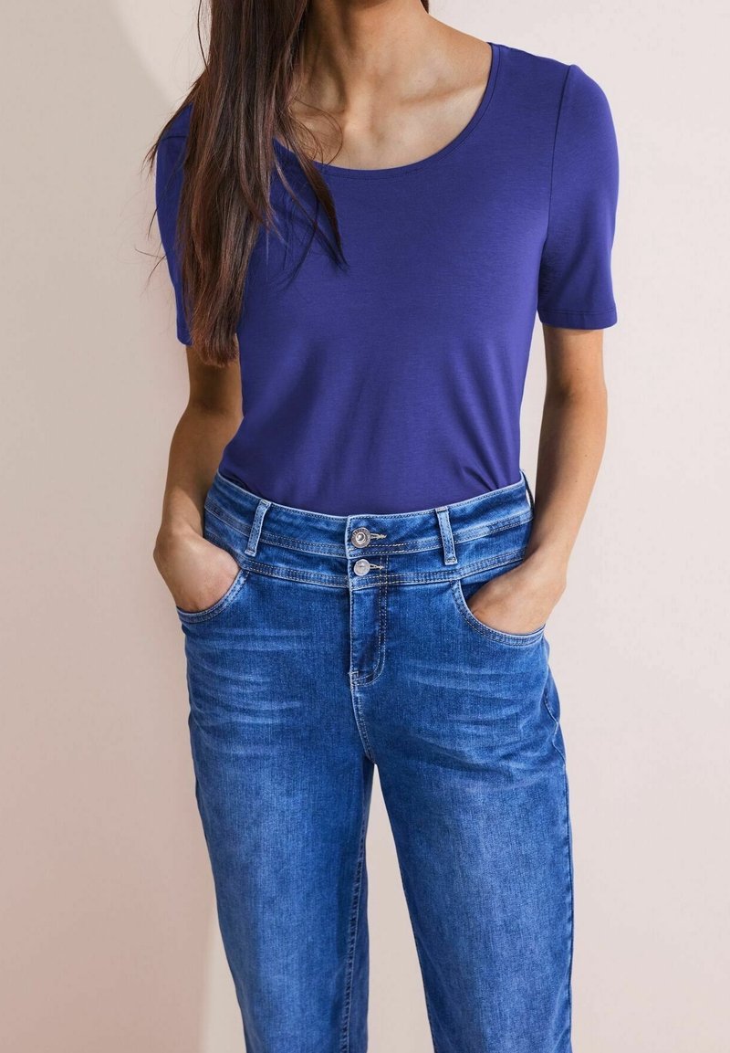 Lila kortärmad topp med rundad halsringning, parat med ljusblå denimjeans med knäppning och framfickor.