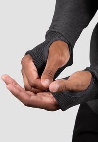 Dark gray, fitted fabric with thumb-hole cuffs. Textured ribbed material at the sleeves and smooth finish on the body. Hands adjusting cuffs.