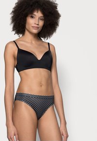 Reggiseno nero con scollatura profonda e spalline sottili; abbinato a slip bikini a vita alta con pois bianchi su sfondo nero.