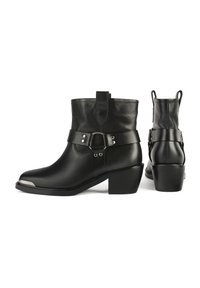 Botas de tobillo de cuero negro con punta redondeada, correa decorativa con acentos metálicos y un tacón grueso. Cuenta con una lengüeta para facilitar su uso.