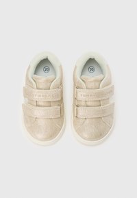 Pantofi aurii pentru copii mici, cu textură și finisaj neted. Două curele cu Velcro și căptușeală ușor căptușită de culoare deschisă. Mărimea 20 este marcată pe talpă.