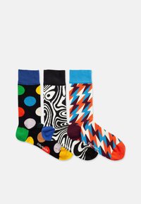 Drei Paar bunte Socken: eins mit schwarzen Polka-Dots, eins mit abstrakten schwarz-weißen Wirbeln und eins mitZickzackmustern in lebhaften Farben.