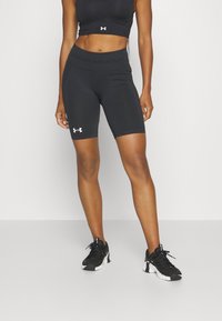 Shorts de sport Under Armour noirs avec un design ajusté, une taille haute et un logo blanc sur la jambe gauche, associés à des baskets noires.