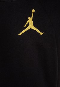 Czarna tkanina z złotym logo Jumpman, przedstawiającym sylwetkę osoby skaczącej z piłką koszykową. Prosty i odważny design.