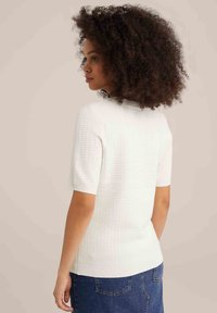 Bílý krátký rukávový žebrovaný top s kulatým výstřihem, s texturovaným vzorem a přiléhavým střihem, kombinovaný s modrými denimovými kalhotami.