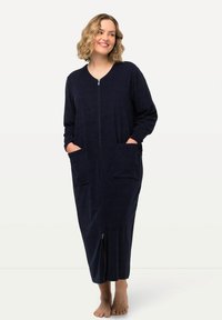 Námořnický modrý dlouhý župan z měkké tkaniny, s předním zipem, dvěma velkými kapsami a dlouhými rukávy. Délka do poloviny lýtek, rovný střih.