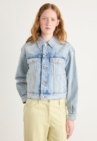 Lichtblauwe spijkerjas met een cropped ontwerp, knoopsluiting, twee borstzakken en een klassieke kraag. De stof vertoont een lichte slijtage.