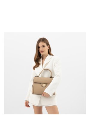 Donna con blazer bianco e pantaloncini che tiene una borsa beige con fibbia dorata su sfondo bianco uniforme.