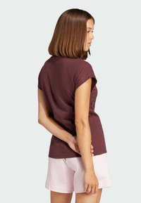 T-shirt corto color bordeaux realizzato in tessuto morbido, abbinato a pantaloni corti rosa chiaro. La t-shirt presenta una vestibilità comoda e un design semplice.