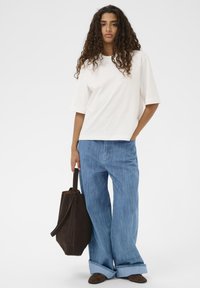 Bela kratka majica s kratkimi rokavi, široke modre denimske hlače, rjava suknja torbica in temno rjavi čevlji s prepognjenimi robovi.