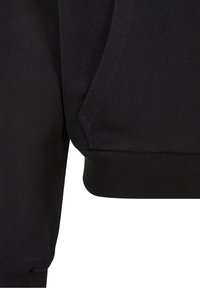 Gros plan sur un tissu de sweat noir, mettant en avant une poche latérale et un ourlet à bords-côtes.