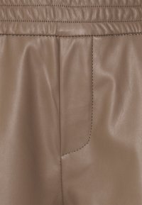 Pantaloni in ecopelle marrone con una texture liscia, cintura elastica e tasca laterale con cuciture a contrasto.