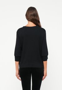 Black long-sleeve top with a relaxed fit. Features a round neckline, rolled-up sleeves, and a smooth texture. Suitable for casual wear.