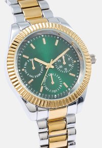 Green dial watch with gold-tone bezel, silver and gold band, and date function. Features three sub-dials and gold hour markers.
