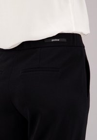 Pantalons noirs avec une texture lisse et une ceinture comportant une petite étiquette de marque. Deux poches arrière avec des ouvertures horizontales.