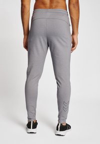 Pantaloni atletici gri cu un design ajustat, talie elastică și detaliu în model chevron negru aproape de glezne, asortați cu adidași negri.