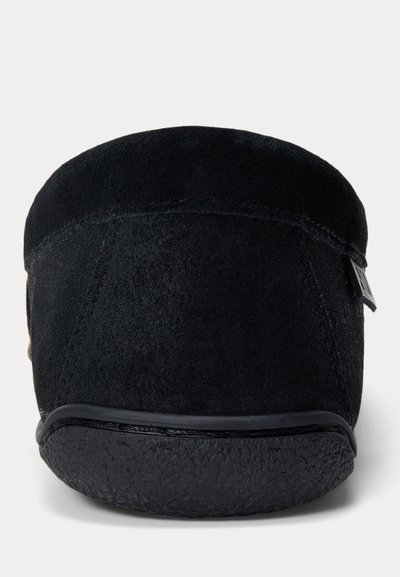 Vue arrière d’une pantoufle en daim noir avec un talon arrondi et une semelle en caoutchouc texturée sur un fond clair uni.