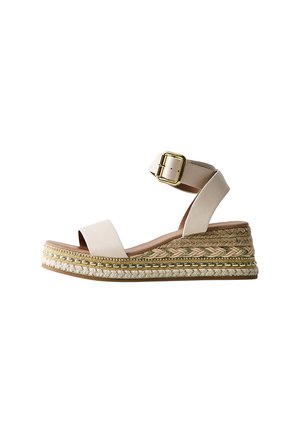 Beige sleehak met enkelriem, gouden gesp en decoratieve gevlochten jute plateauzool.