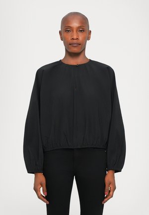 Blusa nera cropped realizzata in tessuto leggero, con maniche lunghe e gonfie, scollatura rotonda e una discreta apertura a chiave frontale.
