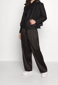 Black textured puffer jacket with hood, layered over a black hoodie, paired with loose gray trousers and white sneakers.