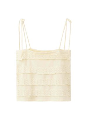 Top court sans manches couleur crème avec détails en dentelle superposée et fines bretelles réglables sur fond blanc.