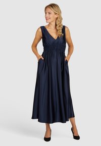 Robe maxi en satin navy avec un décolleté en V, taille smockée et poches latérales ; texture lisse, design sans manches et silhouette fluide.
