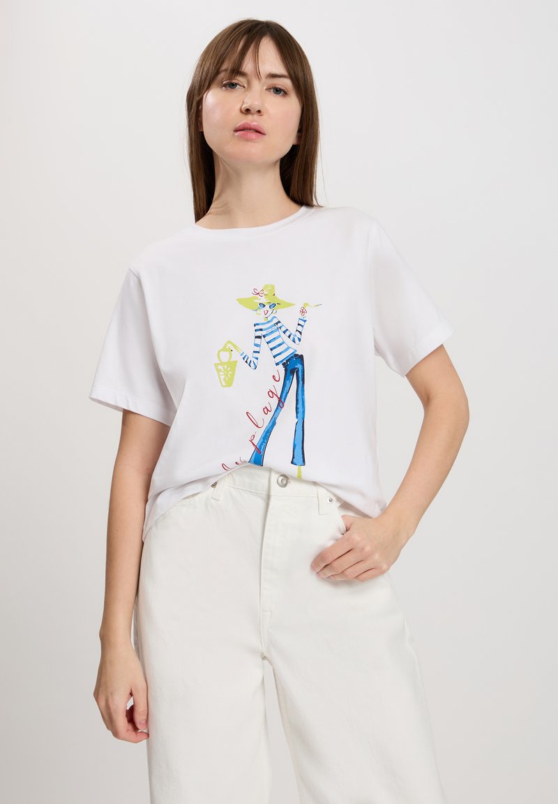 Biała koszulka z bawełny z kolorową grafiką przedstawiającą postać w pasiaku i szerokich niebieskich spodniach. Koszulka ma luźny krój i krótkie rękawy.