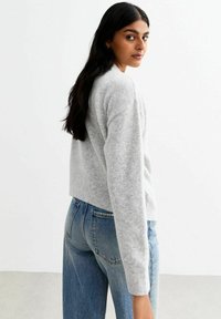 Maglione grigio, corto, realizzato in un morbido tessuto testurizzato con polsini a coste. Abbinato a jeans blu a vita alta, con un taglio classico.