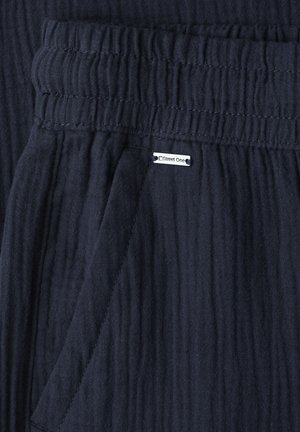 Tissu texturé bleu marine avec taille élastique, couture de poche et petite étiquette blanche de la marque "Street One" cousue près de la poche.