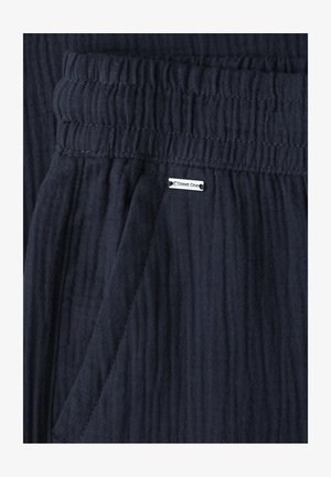 Tissu texturé bleu marine avec taille élastique, couture de poche et petite étiquette blanche de la marque "Street One" cousue près de la poche.