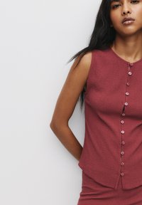 Ribbad, djupt röd ärmlös topp med rundad halsringning, med en rad matchande knappar framtill och utsvängd fåll.