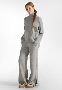 Lichtgrijze gebreide trui met een hoge hals, gecombineerd met bijpassende wijde broek. Heeft zijsplitten en een zachte textuur. Casual en comfortabel ontwerp.