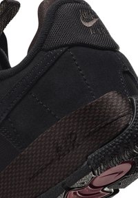 Black athletic shoe featuring a textured upper, mesh accents, and dark brown patterned detailing on the heel. Notable rubber outsole design.