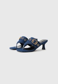 Mules en denim à talons avec un bout pointu, ornés de accents en métal doré et d'œillets décoratifs, dans une couleur bleu profond.