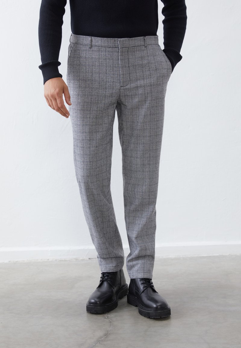 Pantalons à carreaux gris ajustés, avec poches avant, un design plat à l'avant, et accompagnés de bottes noires à lacets.