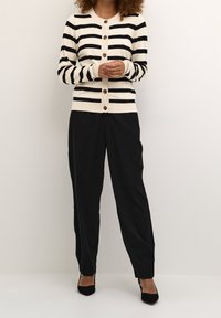 Schwarz-weiß gestreifter Cardigan mit Knöpfen, kombiniert mit schwarzen, schmal geschnittenen Hosen. Strukturierter Stoff, lockere Passform und Rundhalsausschnitt.