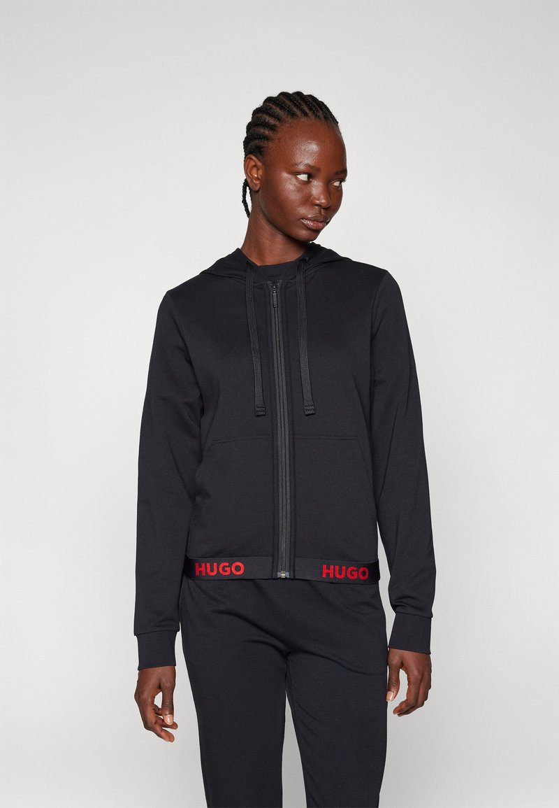 Zwarte rits hoodie van een zachte stof, met een capuchon met trekkoord en een rode "HUGO" logo op de tailleband. Slim fit ontwerp met lange mouwen.