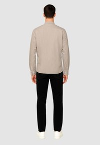 Camicetta beige a maniche lunghe con colletto classico, polsini con bottone e taglio dritto, abbinata a pantaloni neri slim-fit e sneakers bianche.