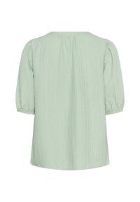 Blouse vert clair en tissu texturé, avec des manches bouffantes à mi-longueur et une coupe ample, présentée de dos sur fond blanc.