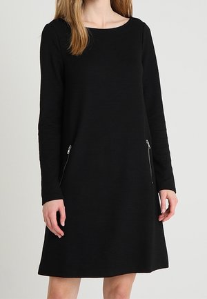 Abito lungo nero con maniche lunghe e scollatura rotonda. Presenta due tasche laterali con zip. Il tessuto è morbido al tatto e l'abito ha una forma a silhouette ad A.