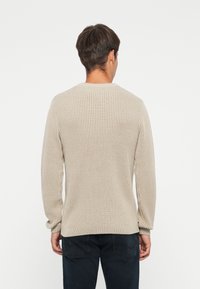 Beige geribde trui met lange mouwen, ronde hals en gestructureerde stof. Geen zichtbare logo's of patronen. Gedragen met donkere spijkerbroek.