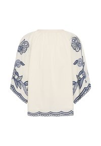 Blouse blanche ample à manches larges, ornée d'une broderie florale bleu foncé complexe sur les manches et l'ourlet, avec des bords festonnés.