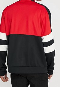 Svart, röd och vit färgblockerad sweatshirt med långa ärmar med vita ränder, hög krage och ribbad nederkant. Mjuk, slät tyg.