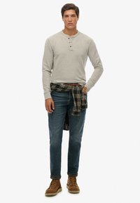 Szara, długą rękawicą henley z trzema guzikami, niebieskie dżinsy, brązowe buty i w kolorową flanelową koszulę w kratkę zawiązaną w talii.