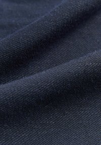 Tmavě námořnická látka s texturovaným, tkaným vzhledem. Povrch ukazuje jemný vzor, který zvyšuje jeho vizuální hloubku a rozměr.