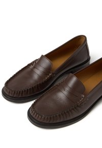 Pair of dark brown leather penny loafers with stitched detailing and black soles on a white background.