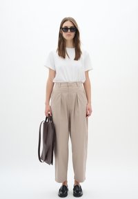 Beige high-waisted trousers, white short-sleeve t-shirt, black sunglasses, and loafers; carrying a dark brown tote bag.