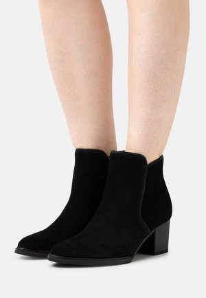 Stivaletti alla caviglia in suede nero con punta arrotondata, pannelli laterali elasticizzati e tacco basso a blocco. Texture liscia e design minimalista.