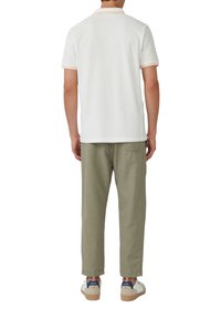 Weißes Poloshirt mit orangefarbenen Akzenten, getragen mit hellgrünen Hosen und weißen Sneakers. Das Shirt hat kurze Ärmel und einen klassischen Kragen.
